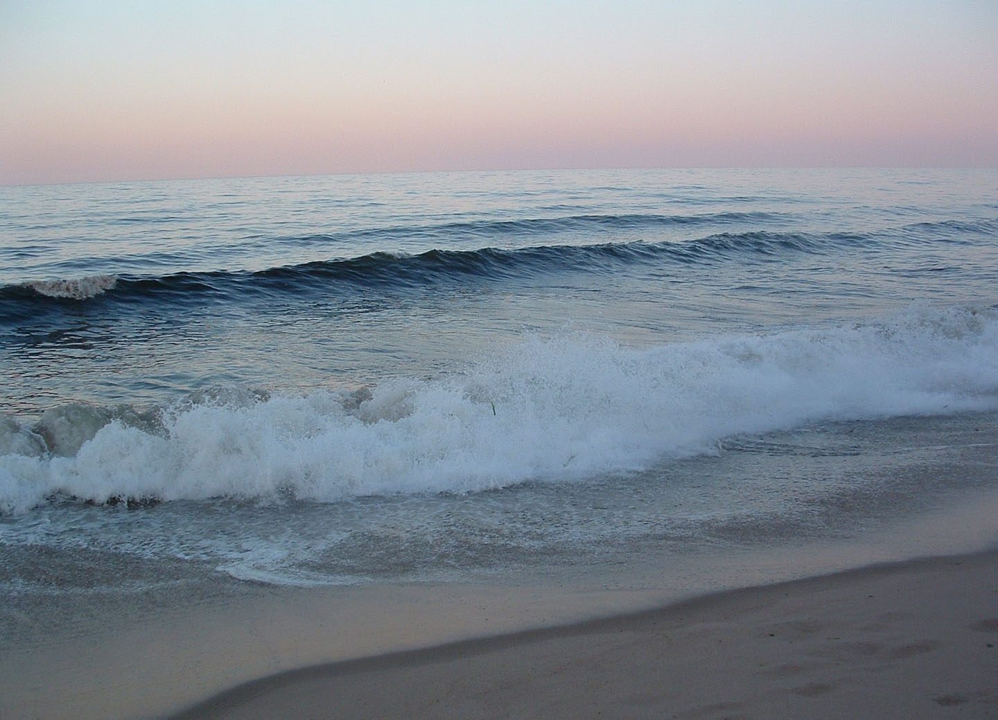 The sky fading from blue to pink as small waves break on the beach