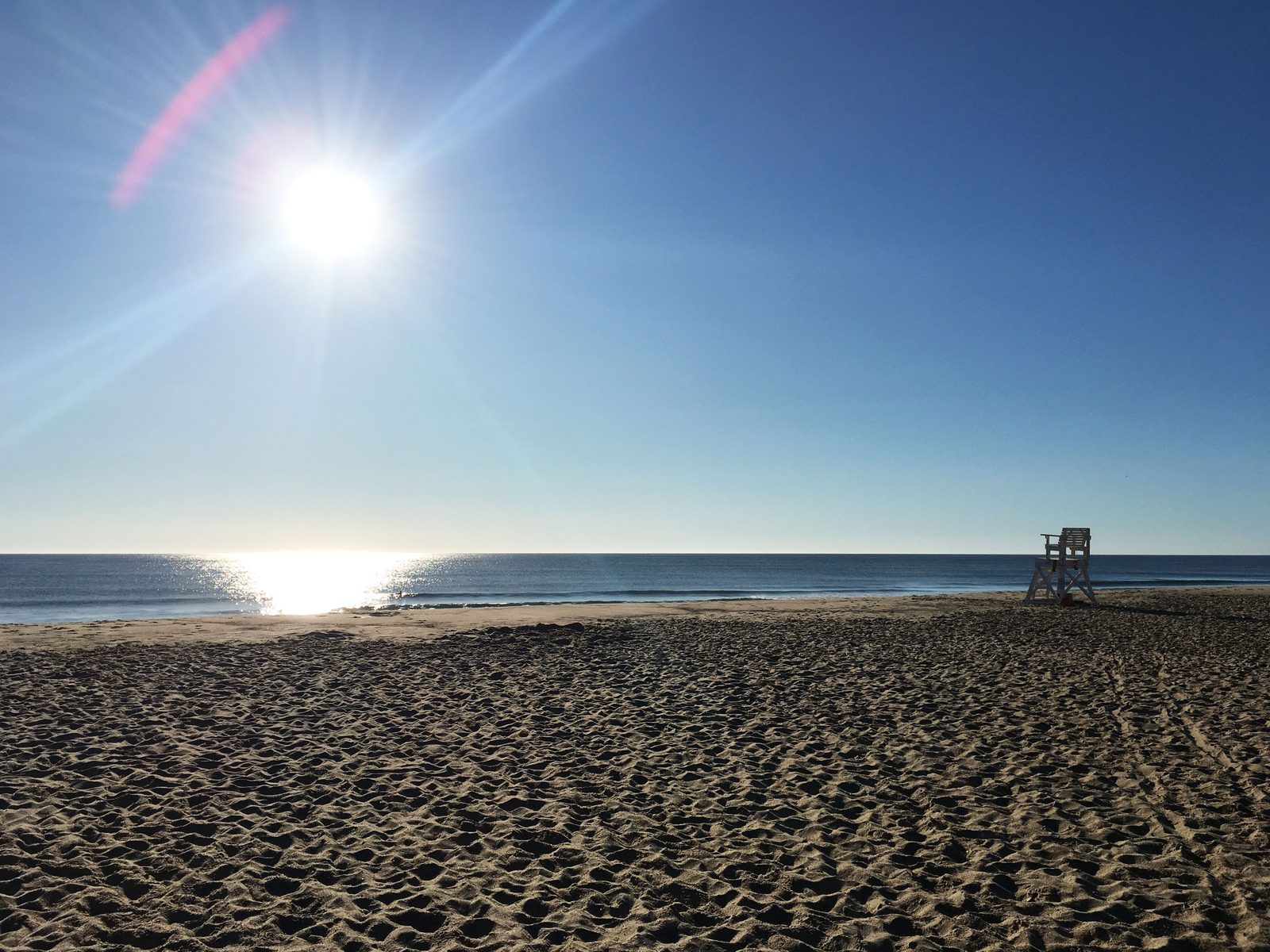 The sun rising over Nauset Light Beach, with a lifeguard chair on the empty sand