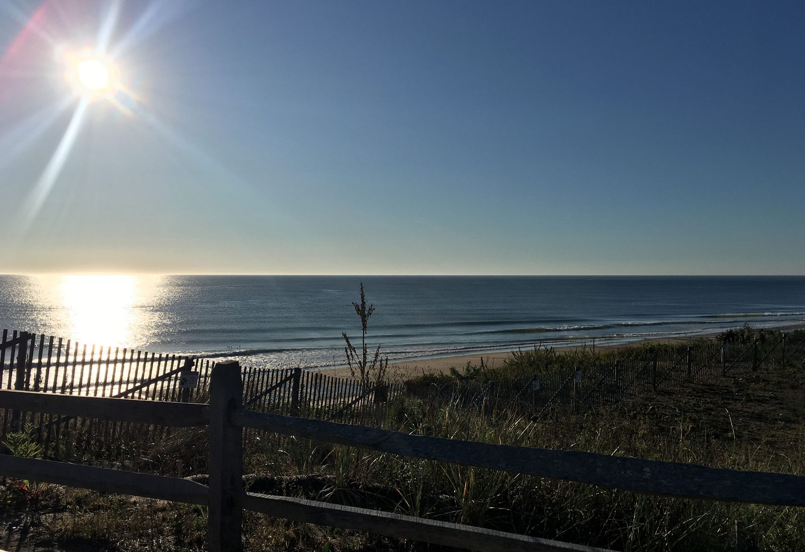 The sun rising over the Atlantic, seen past a dune fence at Nauset Light Beach