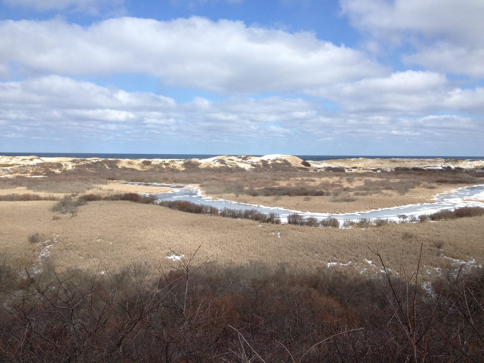 Beige sand dunes rolling toward the water under drifting white clouds