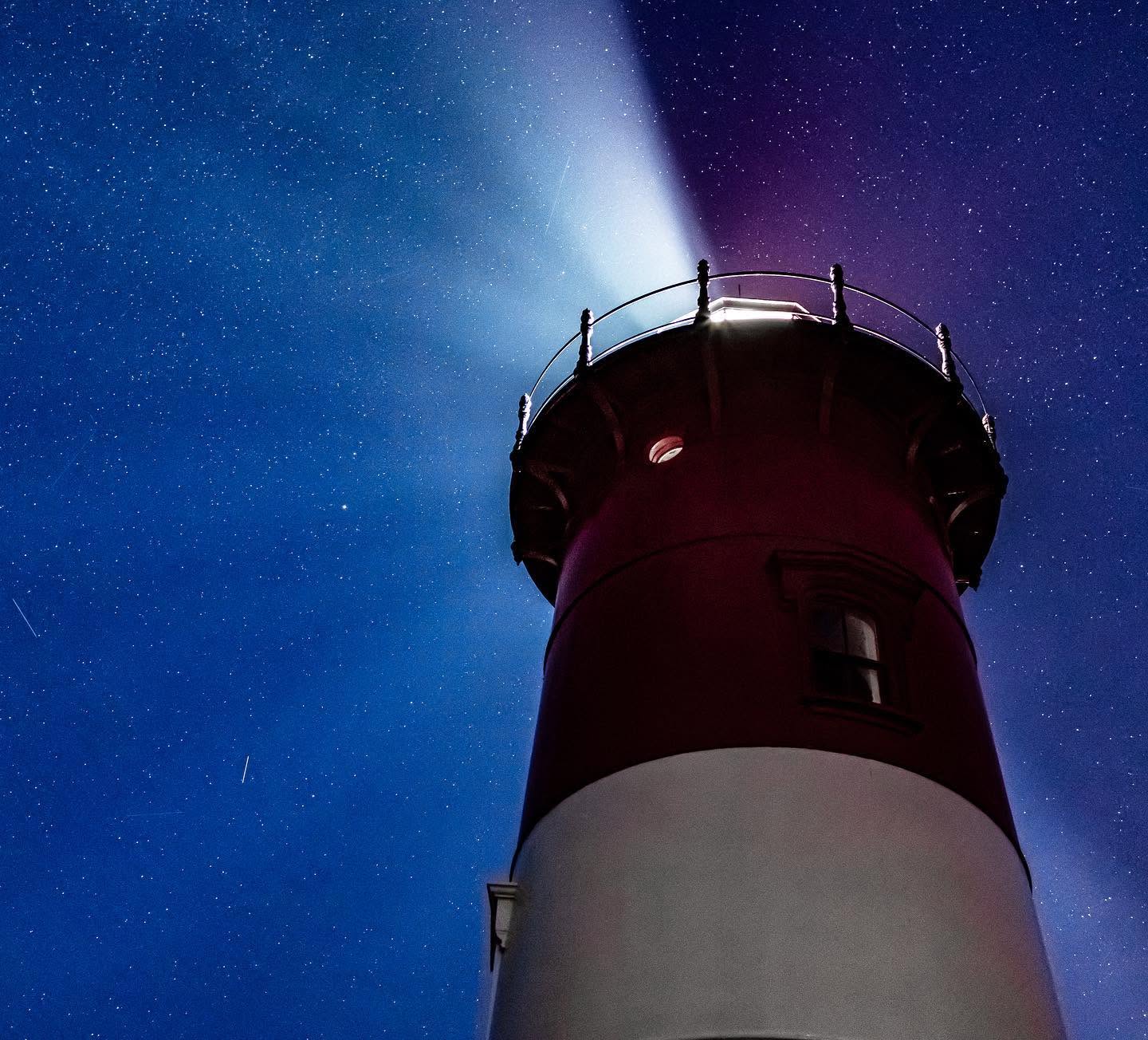 Nauset Light's red and white tower lit against a starry night sky, its beam sweeping the clouds