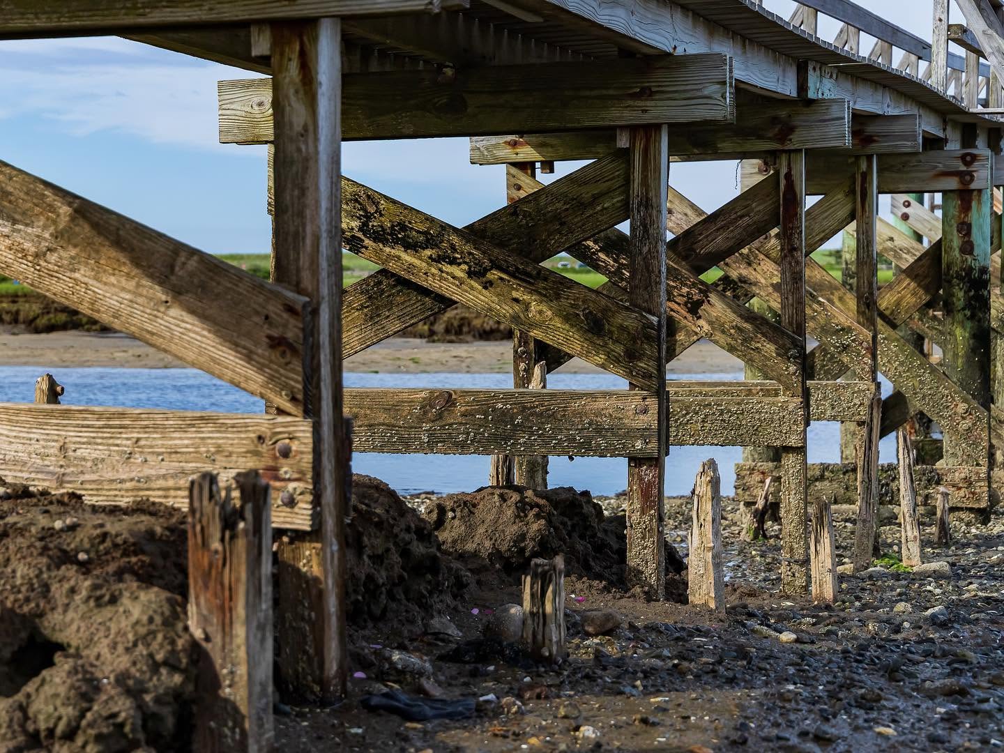 Weathered pilings and cross-braces beneath the Sandwich Boardwalk, with marsh and water beyond
